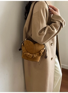 Détail d'un sac seau en daim jaune gingembre en forme de cœur avec volants et pendentif