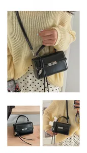 Detail of black crossbody bag with silver clasp, woven charm, and detachable shoulder strap