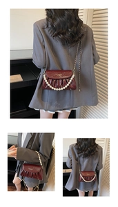 Detail of burgundy ruched faux leather bag with pearl handle and gold chain strap