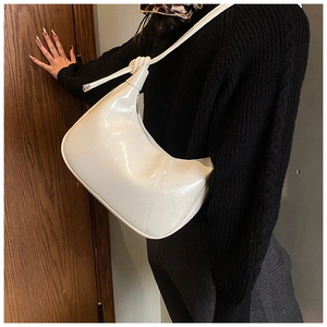 Detail of white glossy crescent moon bag with knotted shoulder strap worn by a model