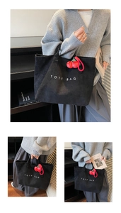 Black matte tote bag with white TOTE BAG text and a 3D red cherry charm detail