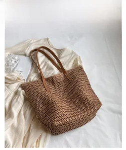 Gros plan d'un sac cabas en paille kaki avec poignées en cuir marron pour les vacances