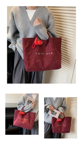 Detail of burgundy suede tote bag with white text and a red cherry charm accessory
