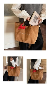 Detail of a brown corduroy tote bag with TOTF BAG text and red cherry charm accessory