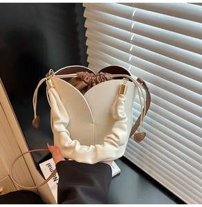 Détail du sac seau tulipe avec poignée plissée et pendentif coeur sur cuir crème