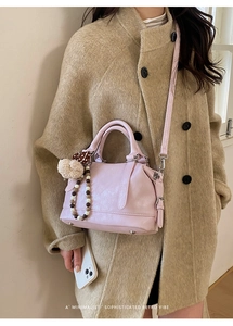 Detail of light pink Boston bag with fuzzy pompom and beaded charm on khaki wool coat