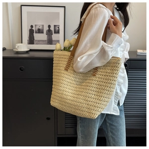 Détail d'un sac cabas tissé beige avec des bretelles en cuir marron et coutures en croix
