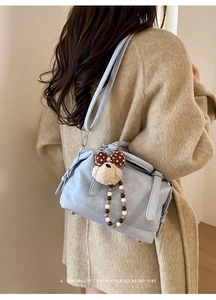 Detail view of a blue Boston bag featuring a plush dog charm and beaded strap on a wool coat