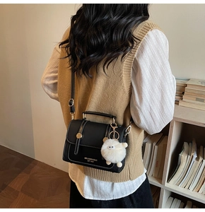 Detailed side view of black leather crossbody bag with white stitching and plush sheep charm