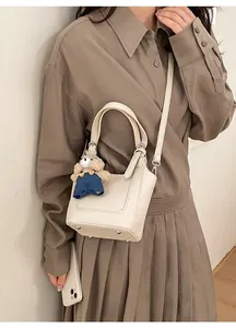 Close-up of cream white lychee leather bucket bag with bear charm and bottom metal studs