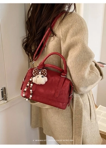 Detail of red retro Boston bag with bear pendant and beaded handle on a model's shoulder