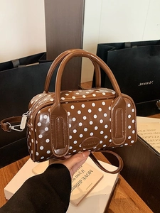 Brown Boston handbag with white polka dots featuring dual handles and a long strap