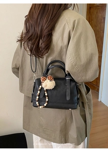 Close-up of black retro Boston bag with plush dog charm and beaded chain detail