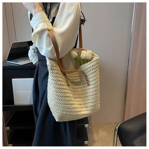 Détail d'un grand sac cabas en paille beige avec anses en cuir marron et fleurs