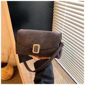 Gros plan d'un sac bandoulière marron foncé mat avec boucle dorée rectangulaire sur le rabat