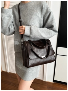 Detail of dark brown leather crossbody bag featuring textured finish and sturdy handles