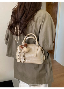 Minimalist beige Boston bag with plush lamb charm shown on model in a retro setting