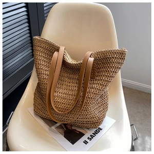 Détail d'un sac cabas en paille tissée avec anses en cuir marron sur une chaise