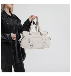Detail of ivory faux leather tote bag showing side pockets and metal hardware accents