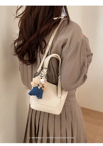 Detail view of a cream bucket bag with lychee texture leather and a cute bear charm