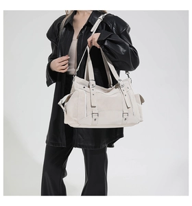 Detail of a large white fashion tote with multiple zippers and metallic hardware buckles
