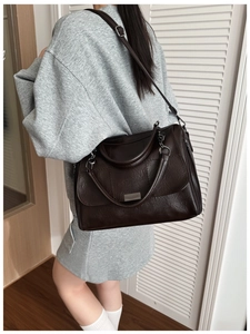 Detail of a dark brown pleated leather shoulder bag with silver metal plaque and strap