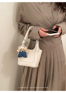 Detail of cream-colored bucket bag with leather texture and cute teddy bear pendant