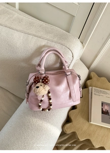 Detail of soft pink Boston handbag with cute bear charm on a stylish white sofa