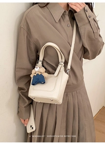 Close-up of cream leather bucket bag showing metal feet and a cute plush bear charm