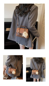 Detailed view of a retro saddle bag with contrast stitching and decorative cream pompom charm