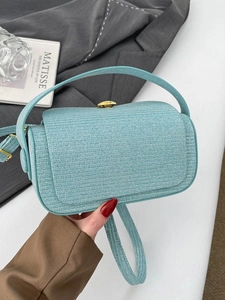 Fashion light blue woven textured square handbag with a gold clasp held against a blazer