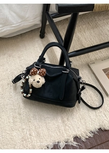 Detail of black Boston bag featuring a white plush puppy charm and beaded chain
