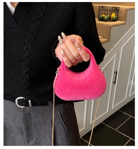 Detail of pink geometric textured handbag with gold chain held by a model in casual wear