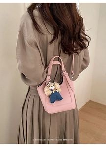 Detailed close-up of a pink pebbled leather bucket bag with a cute curly dog plush charm