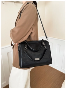 Close-up of a black quilted shoulder bag with chain strap worn by a model in a brown suit