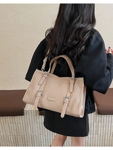 Detail of beige pleated tote bag featuring silver buckles and adjustable shoulder strap