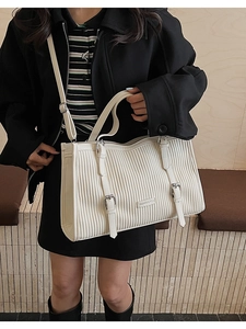 Detail of cream tote bag with vertical pleats and adjustable shoulder strap worn by model