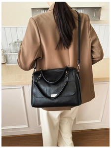 Detail of a black quilted tote bag with silver metal plaque on a caramel blazer model