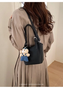 Black litchi leather bucket bag shown on model with a cute plush bear pendant