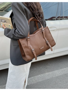 Close-up of brown textured leather tote bag with vertical stripes and metal logo plate