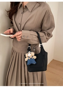 Detail of black lychee leather bucket bag with silver buckle and plush bear charm