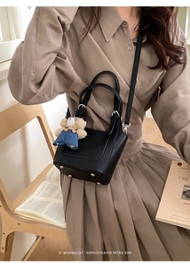 Close-up of black litchi pattern leather bucket bag with cute bear charm on wooden chair