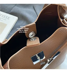 Close-up of the silver magnetic snap closure and textured leather strap on a brown bucket bag