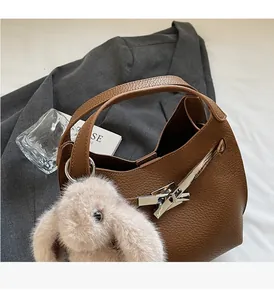 Close-up of brown lychee leather bucket bag with metal buckle and plush rabbit charm