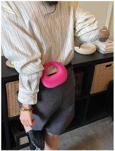 Detail of rose red ring-shaped handbag with gold chain on model in home setting