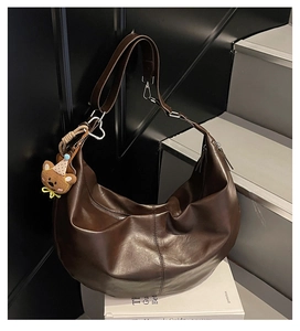 Detail of dark brown leather crescent bag with plush bear charm on a minimal background