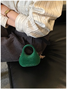 Detail of green quilted mini crescent handbag with gold chain strap on black leather background