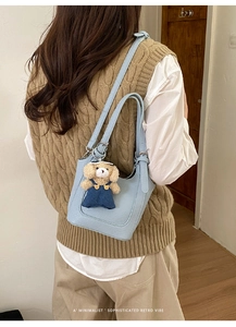 Detail of light blue bucket bag with pebble texture and cute teddy bear charm
