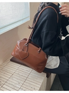 Detail of brown vintage shoulder bag featuring heart charm and knotted strap design
