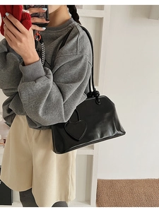 Detail of black glossy faux leather tote bag with heart charm and knotted straps